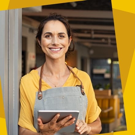 A woman business owner in an apron holding a tablet.