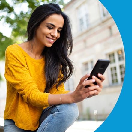 A young woman smiling while using a smartphone.