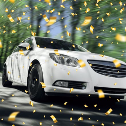 Side-panel view of a white sports car with confetti flying around it.