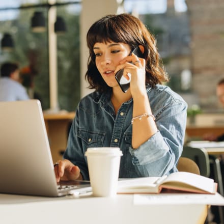 A woman on her mobile device looking at her laptop.