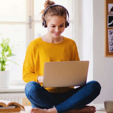 A young adult female on her laptop with headphones.