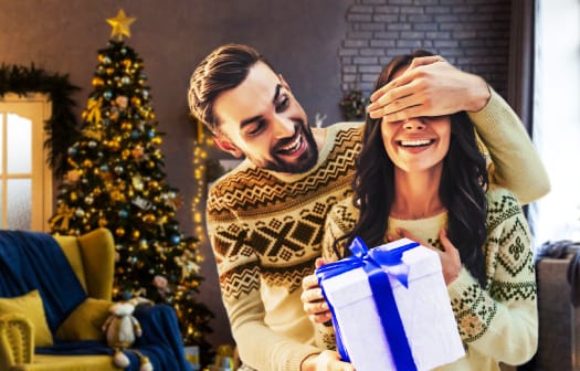 A young couple opening a holiday present in front of a christmas tree.