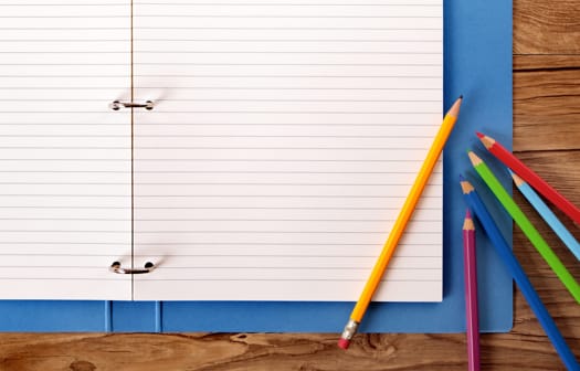 An open folder with blank ruled paper and colorful pencils laying on top of it.