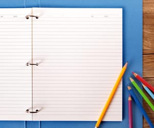 An open folder with blank ruled paper and colorful pencils laying on top of it.
