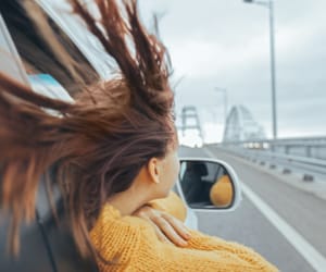 A woman hanging outside the passenger window of a car with her hair blowing in the wind.