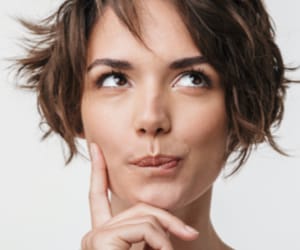 A woman pondering with her finger pressed against her cheek.