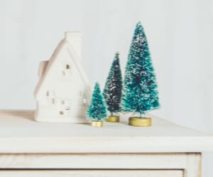 Small scale christmas trees and a cottage resting on a white table.