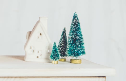 Small scale christmas trees and a cottage resting on a white table.