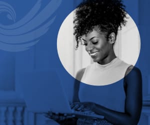 A young professional woman standing while using a laptop.