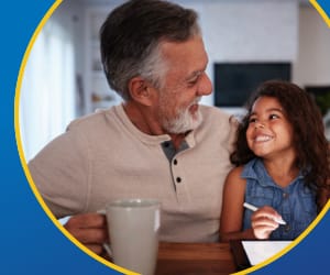 A grandfather happily holding his granddaughter while drinking coffee.