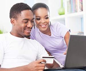 A smiling couple with one holding a credit card and the other looking at a laptop