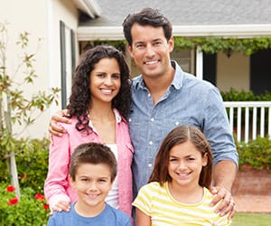 A family of two smiling and standing together on the lawn of their home