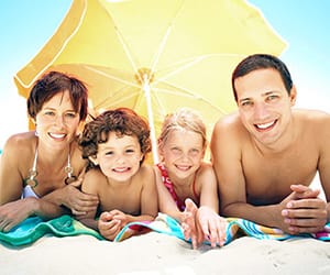 A family of two kids smiling at the beach under a yellow umbrella