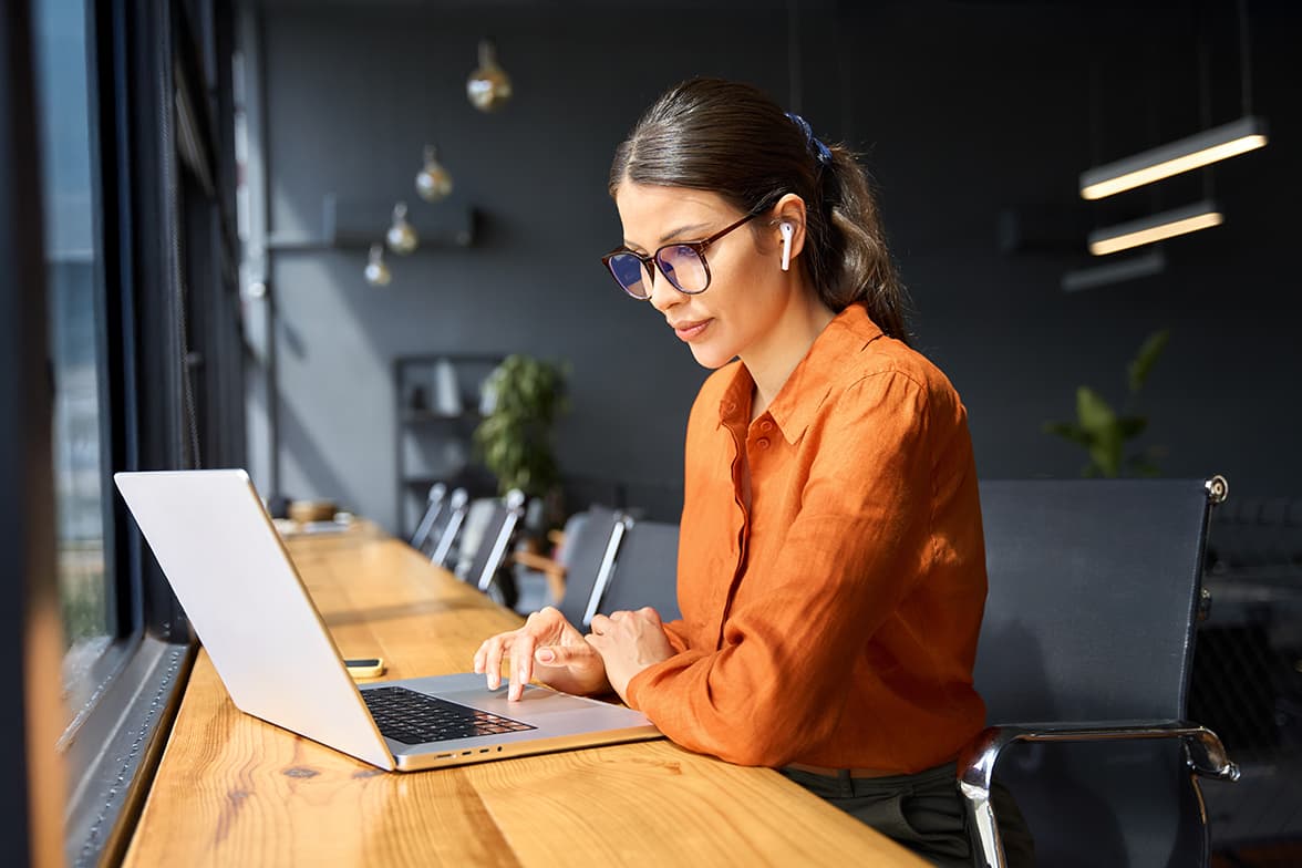 A young, professional woman sitting at a desk working on a laptop.