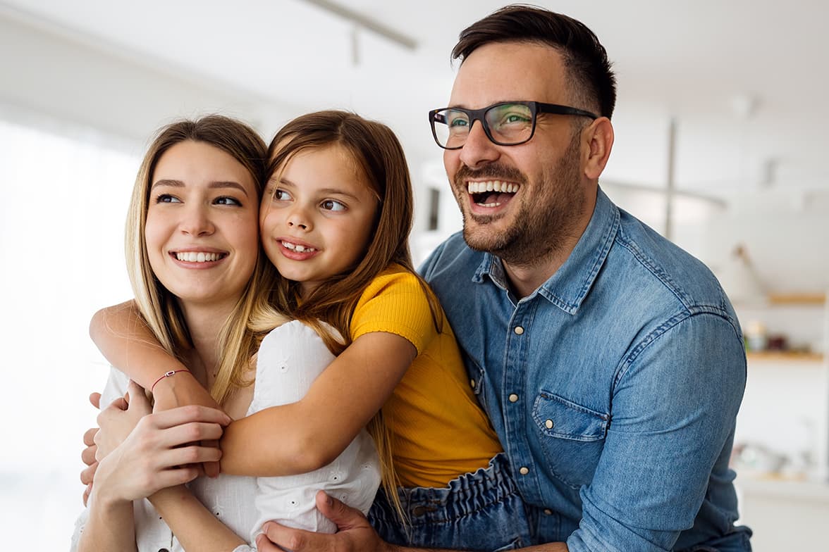 A father and two daughters smiling and embracing eachother.
