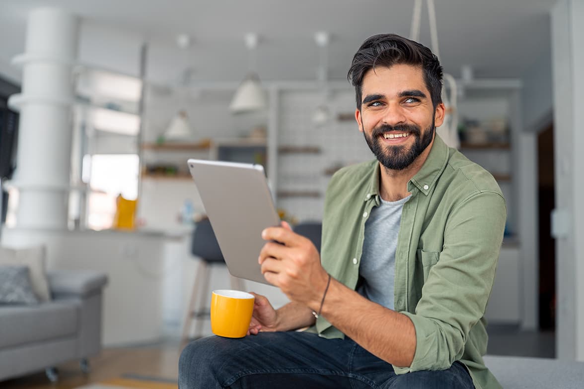 A man sitting while holding a tablet and a mug.