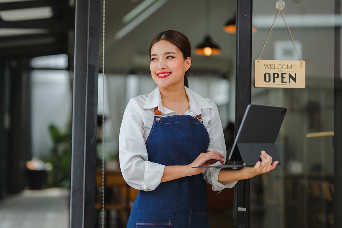 A hostess standing in front of a restaurant holding a laptop.