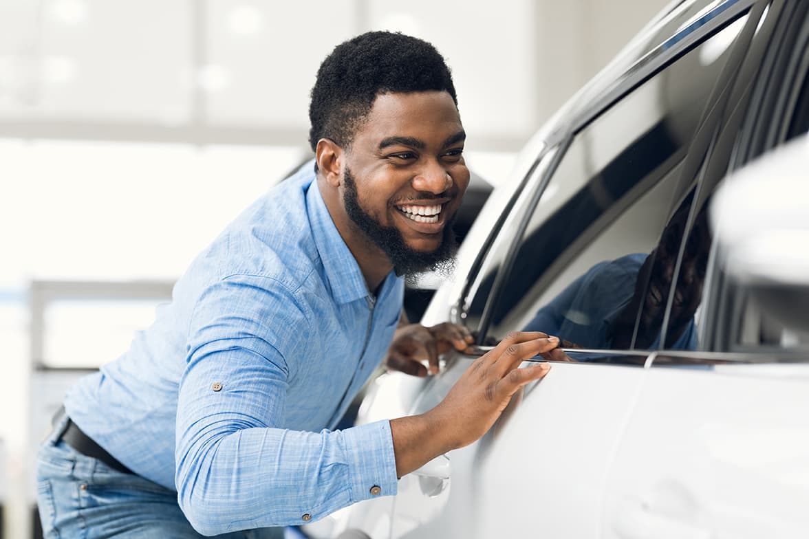 A happy, young man looking into the passenger side of a car.