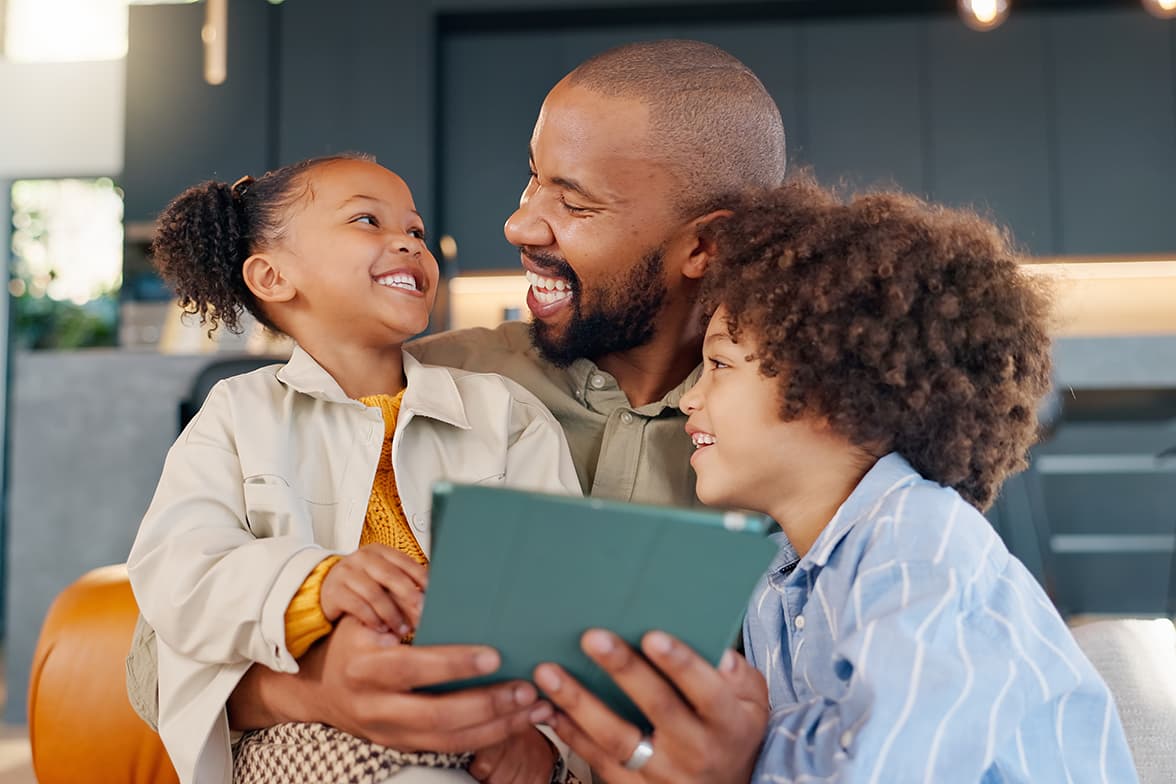 A father holding two children while looking at a tablet.