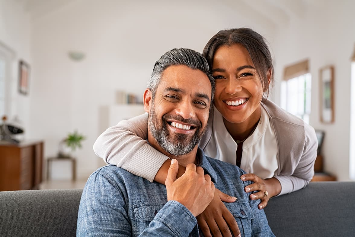 A middle-aged couple sitting on a couch together smiling.