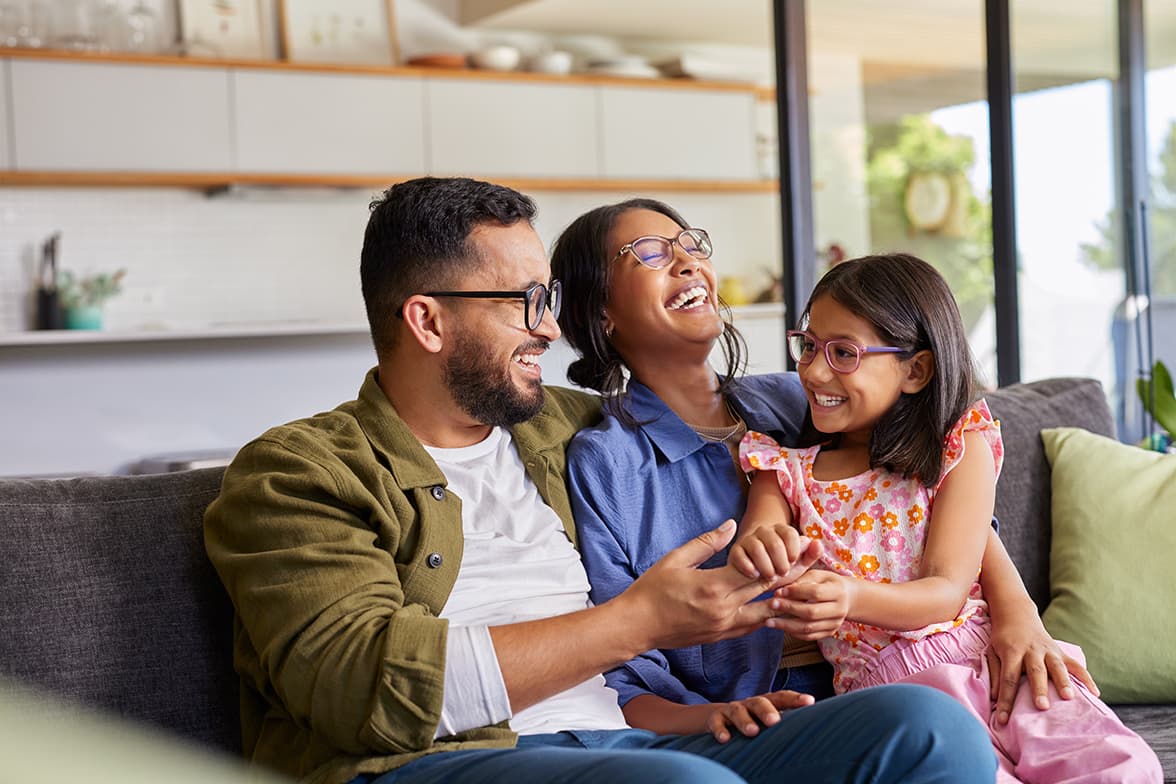 A family of three laughning and sitting on a couch together.