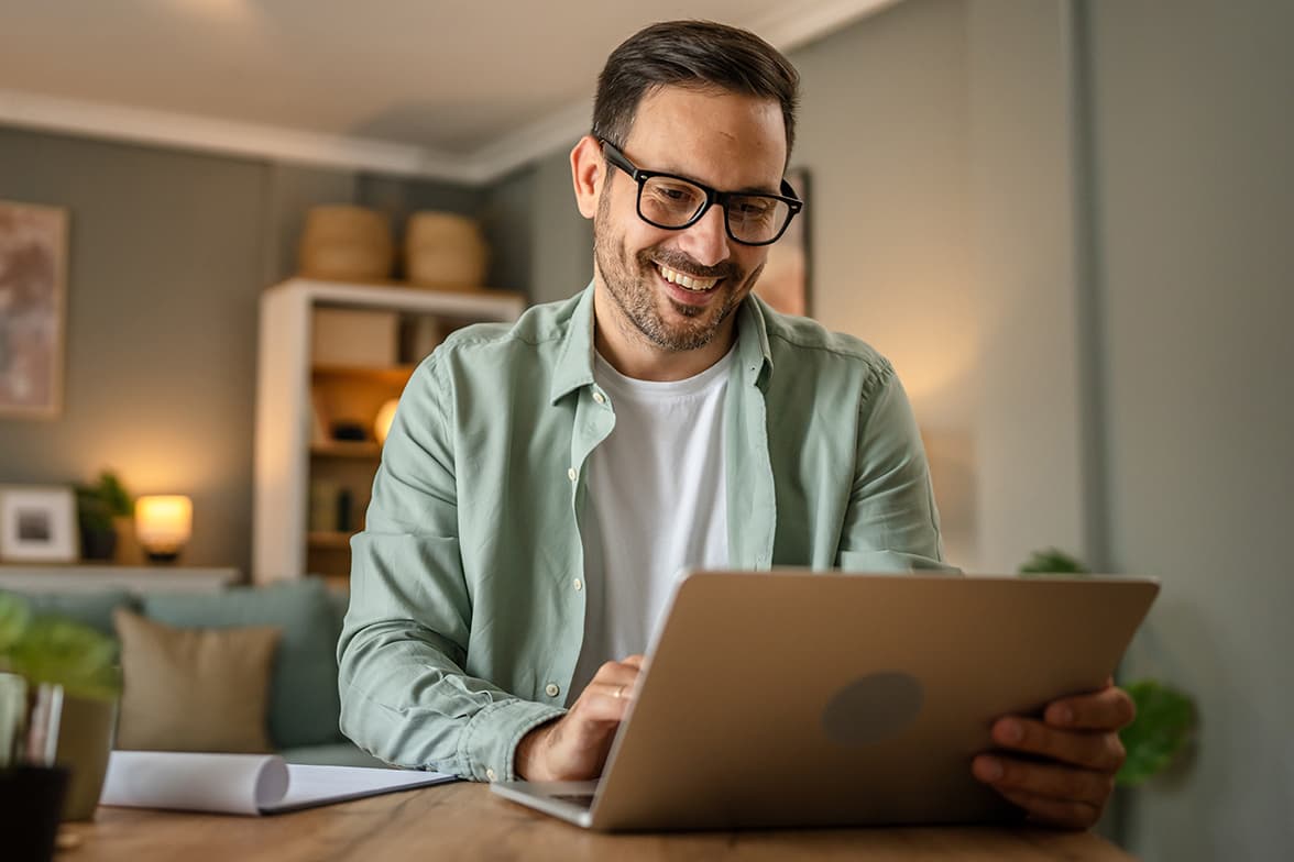 A man sitting at a table looking at a laptop.