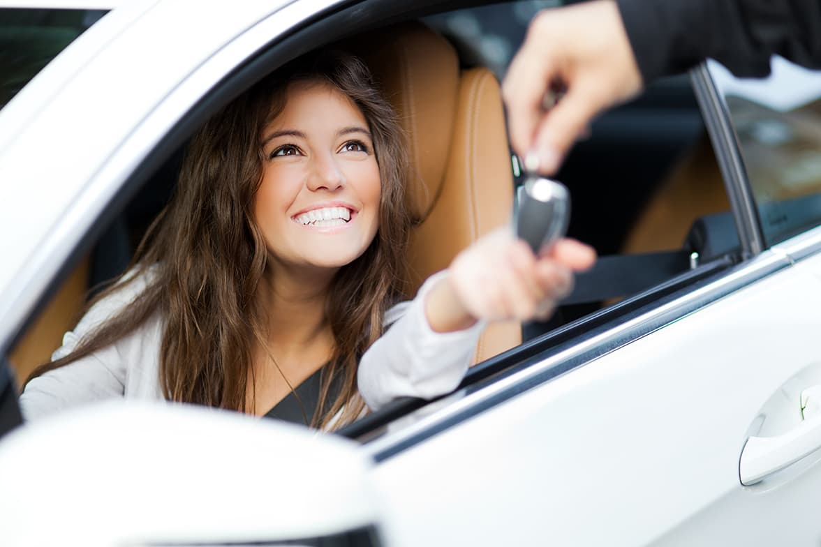 A young woman in the driver's seat of a car reaching for keys.