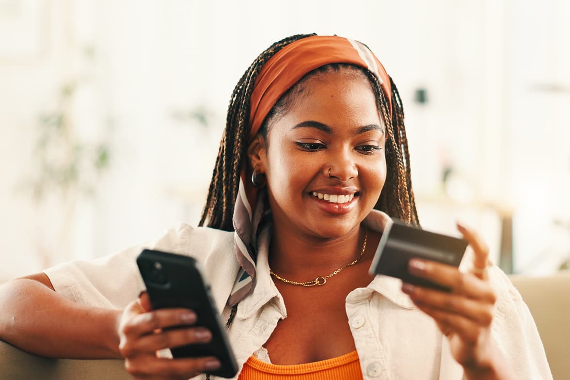 A young woman holding a smart phone and a credit card.