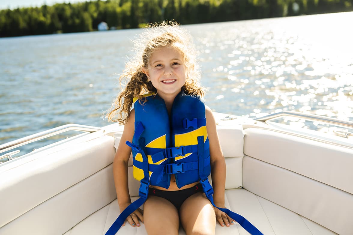 A smiling, young girl sitting in a boat wearing a life jacket.