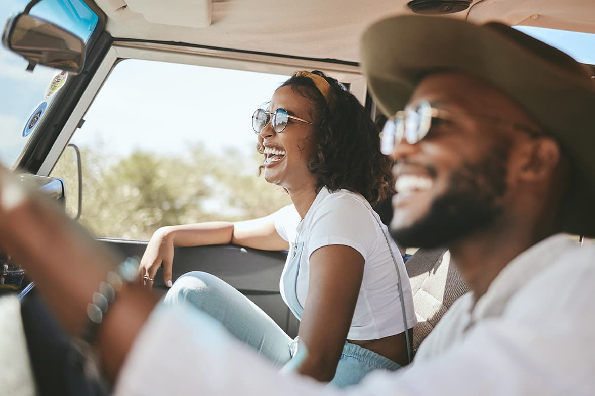 A happy couple driving in a car on a sunny day.