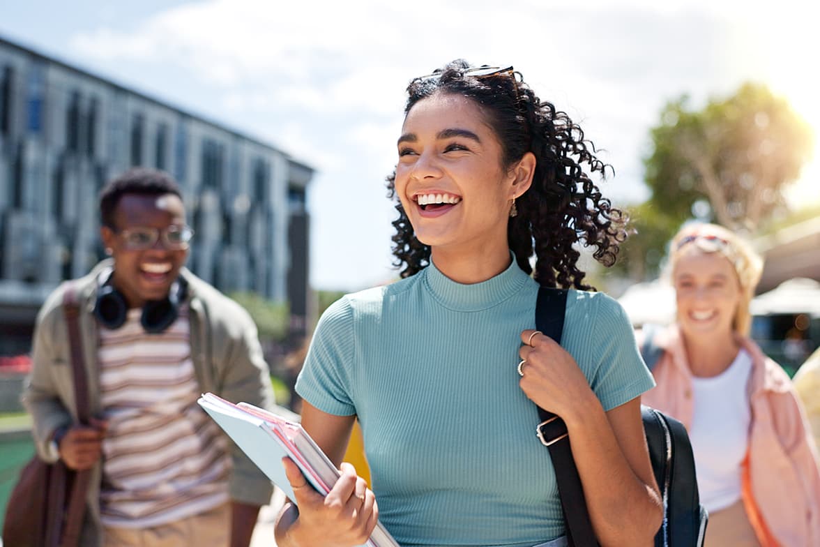 Three joyful high school students walking with book bags.