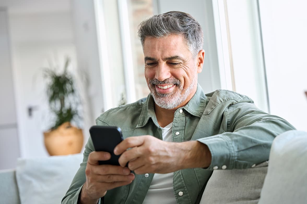 A middle-aged man siting on a couch using a smart phone.