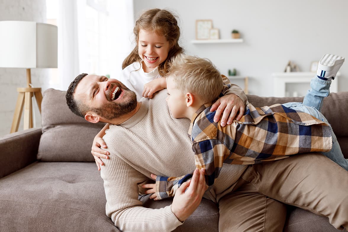 A man playing with two children on a couch.