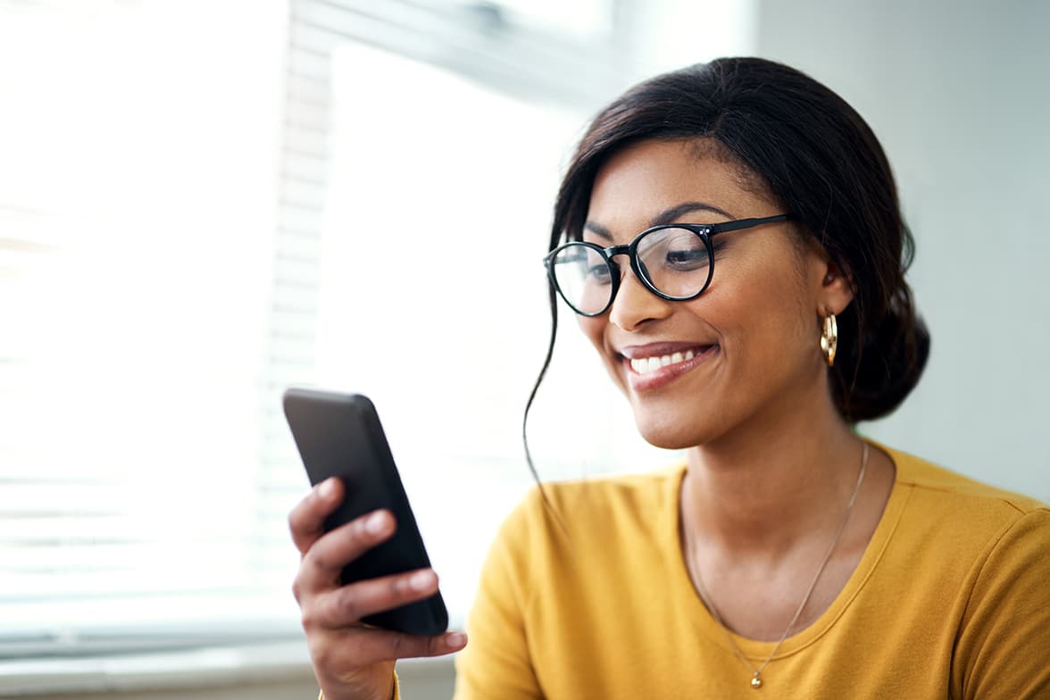 A young, smiling woman holding and looking at a smartphone.