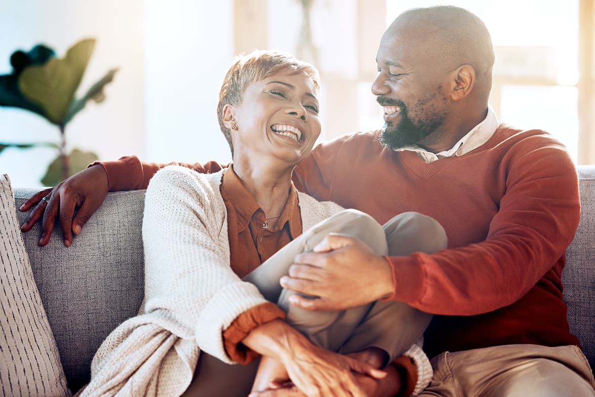 A middle-aged couple sitting on a couch laughing.