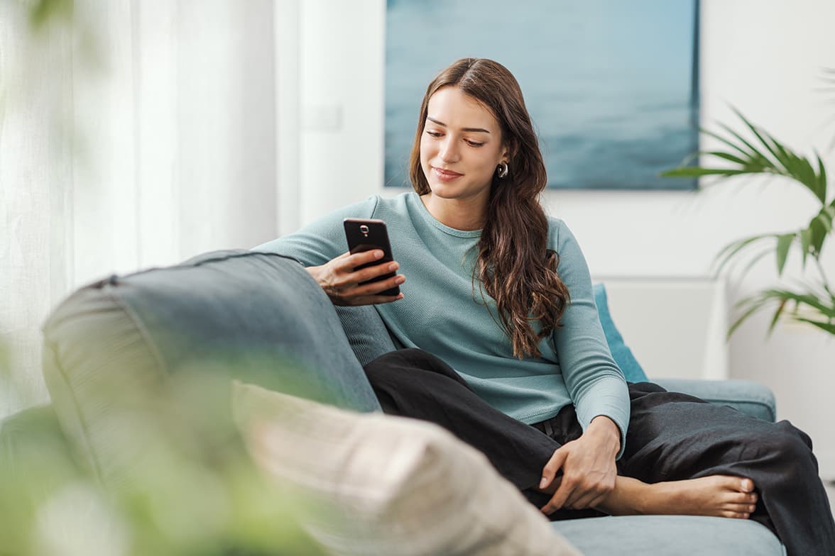 A young woman sitting on a couch using a smartphone.