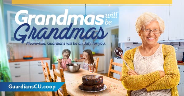 A happy grandmother standing in front of a kitchen table with grandkids in the background eating a freshly made chocolate cake.