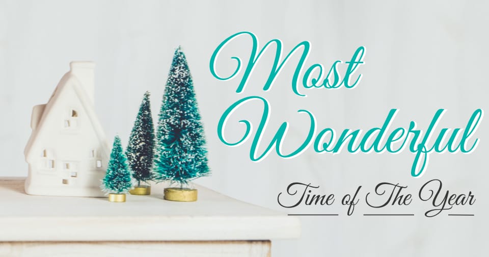 Small scale christmas trees and a cottage resting on a white table. To the right, the words: most wonderful time of the year.