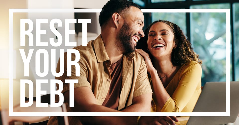 A couple smiling at each other sitting in front of a laptop. The words on the left: reset your debt.