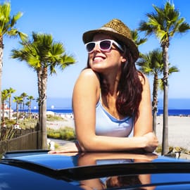 Woman smiling and wearing sunglasses while standing through the sunroof of a car