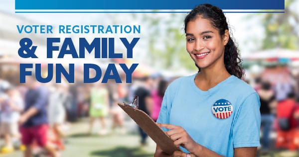 A young woman holding a clipboard with a VOTE button pinned to her t-shirt.