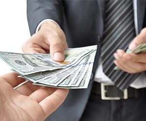 A man in a suit handing over several $100 bills