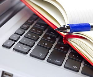 An open notebook with a blue pen on top of a laptop