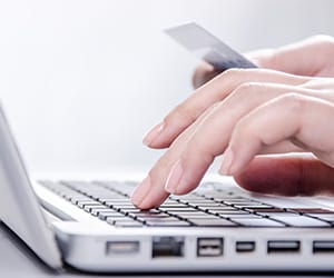 Hands typing on a laptop and holding a card